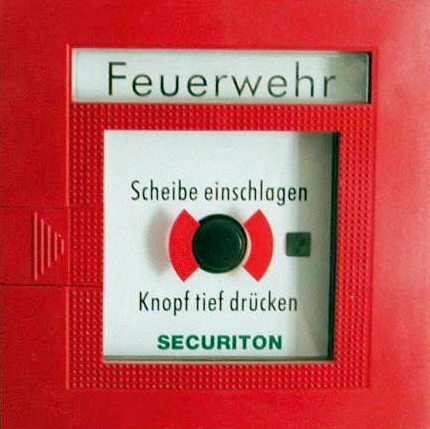 Feuermelder mit der Aufschrift „Feuerwehr“ und der Anweisung „Scheibe einschlagen, Knopf tief drücken“